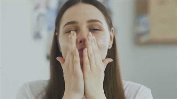 Mujer aplicando mascarilla hidratante crema para la piel en la cara y mira a la cámara — Vídeos de Stock