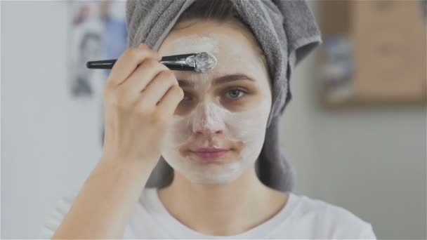 Mulher com toalha na cabeça aplicando máscara cosmética e olhar para a câmera — Vídeo de Stock
