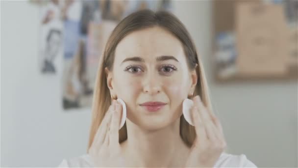 Młoda kobieta czyszczenie twarzy z płatki kosmetyczne i spojrzeć na kamery — Wideo stockowe