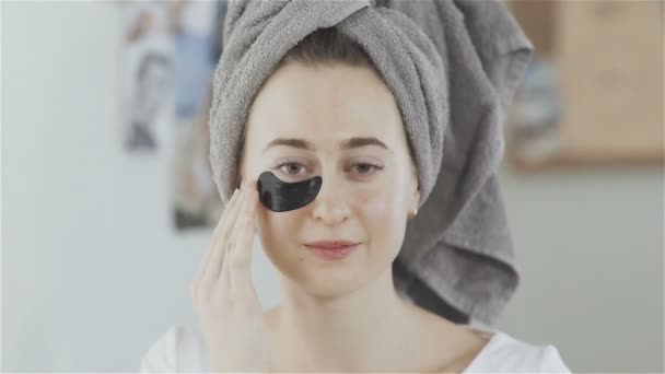 头上有毛巾的妇女在眼睛下面施加了一个清爽的胶原蛋白保湿面膜的补丁. — 图库视频影像
