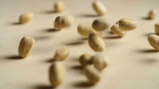Pimpernoten (pistaches) vallen op een houten achtergrond in slow motion — Stockvideo