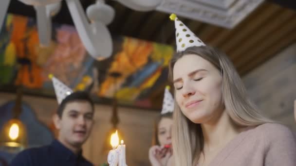 Joven rubia está pidiendo deseos y soplando velas encendidas en pastel de cumpleaños — Vídeo de stock