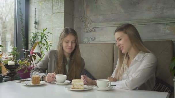 To vakre, unge kvinner som drikker kaffe og spiser kaker på kafeen – stockvideo