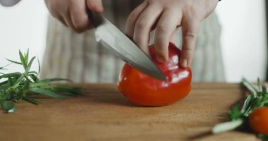 Büyük bir kırmızı tatlı biber bir kesme tahtası üzerinde kesilir.