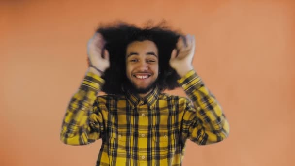 Hombre afro-americano preocupado riendo, manteniendo las manos en su cara y celebrando el éxito en el fondo naranja . — Vídeos de Stock