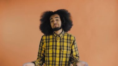 Çaresiz Afro-Amerikan bir adamın portresi. El ele tutuşup omuz silkiyor. Turuncu arka planda yardım edemiyor. Duyguların kavramı