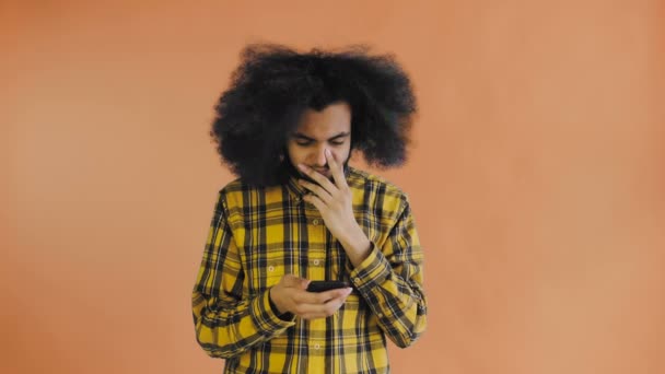 Joven hombre afro-americano triste usando el teléfono y recibiendo malas noticias en el fondo naranja. Concepto de emociones — Vídeos de Stock