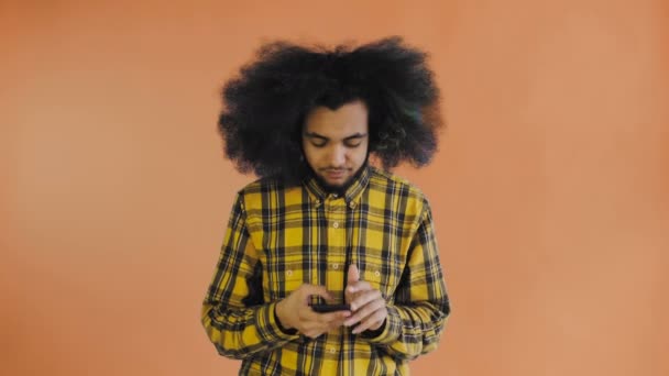 Znechucený mladý Afroameričan držící rozbitý mobil na oranžovém pozadí. Pojetí emocí — Stock video