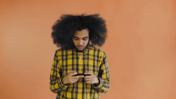 Uomo afro-americano Gioco su Smartphone su sfondo arancione. Concetto di emozioni — Video Stock