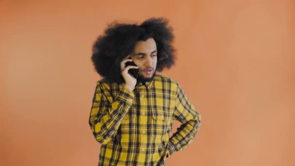 Feliz atraente jovem afro-americano falando no celular em fundo laranja. Conceito de emoções — Vídeo de Stock