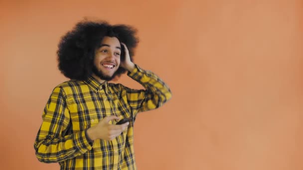 Felice attraente giovane afro-americano utilizzando il telefono e ottenere buone notizie su sfondo arancione. Concetto di emozioni — Video Stock