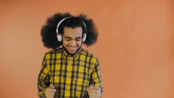 Positieve Afro-Amerikaanse man die muziek luistert in zijn koptelefoon op Orange achtergrond. Concept van emoties — Stockvideo