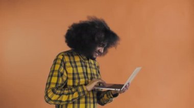 Afro-Amerikalı adam dizüstü bilgisayarda yazıyor ve turuncu arka planda gülümsüyor. Duyguların kavramı
