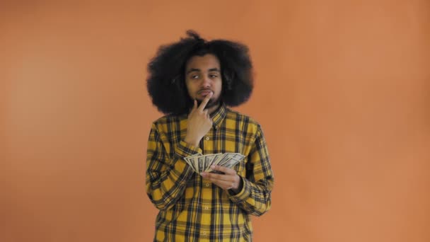 Uomo afroamericano in possesso di denaro nelle sue mani e pensando a qualcosa su sfondo arancione . — Video Stock