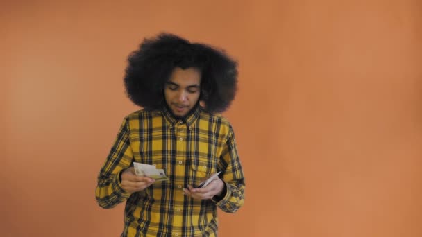 Giovane uomo afroamericano contando denaro contante su sfondo arancione . — Video Stock