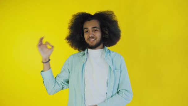 黄色の背景の上に隔離された立っている間、 ［OK］をジェスチャーを示す魅力的なアフリカ系アメリカ人の男を笑顔。感情の概念 — ストック動画