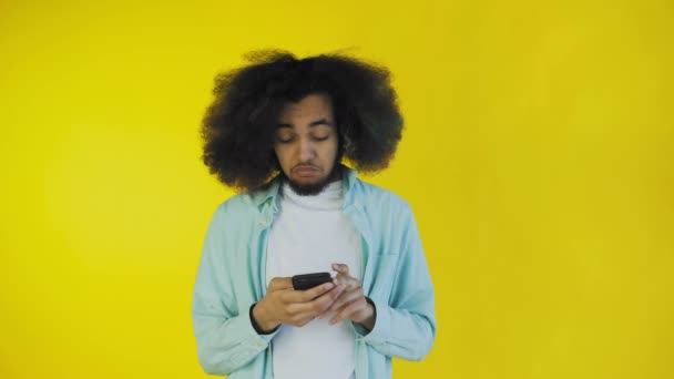Giovane afro-americano che usa il telefono e riceve buone notizie su sfondo giallo. Concetto di emozioni — Video Stock