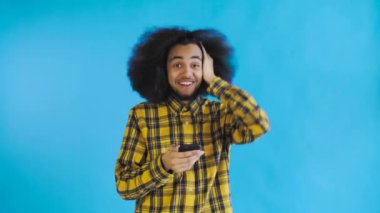 Genç mutlu Afrikalı işadamı telefonu kullanıyor ve Mavi arka planda iyi haberler alıyor. Duyguların kavramı