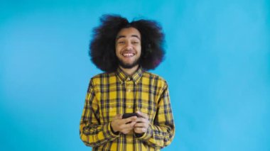 Genç mutlu Afrikalı işadamı telefonu kullanıyor ve Mavi arka planda iyi haberler alıyor. Duyguların kavramı