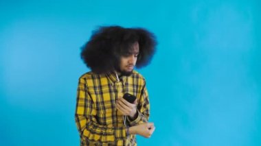 Mavi arka planda kulaklıkla müzik dinlemek için telefonu kullanan Afro-Amerikan bir adam. Duyguların kavramı