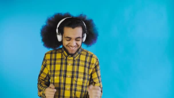 Θετικός Αφροαμερικάνος ακούει μουσική με τα ακουστικά του σε μπλε φόντο. Έννοια των συναισθημάτων — Αρχείο Βίντεο