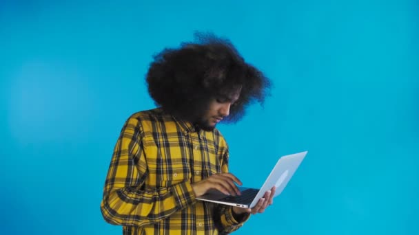 Gelukkige Afro-Amerikaanse man met laptop op blauwe achtergrond. Concept van emoties — Stockvideo