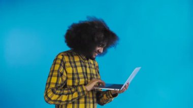 Afro-Amerikalı adam dizüstü bilgisayarda yazıyor ve mavi arka planda gülümsüyor. Duyguların kavramı