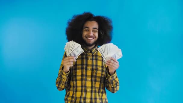 Jovem afro-americano segurando dinheiro em dinheiro em fundo azul . — Vídeo de Stock