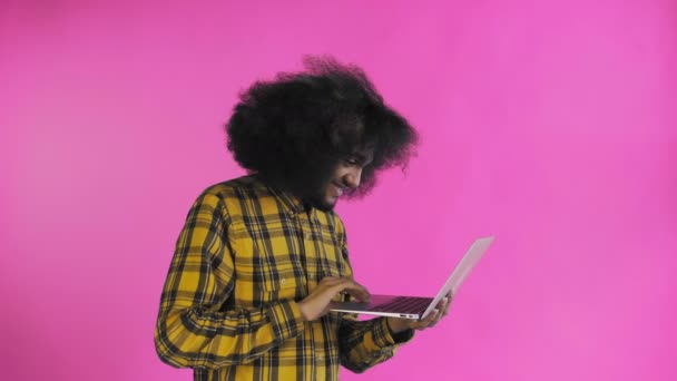 Uomo afroamericano che digita al computer portatile e sorride su sfondo viola. Concetto di emozioni — Video Stock