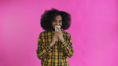 Elinde para tutan ve mor arka plandaki kameraya bakan mutlu Afrikalı genç bir Amerikalı..