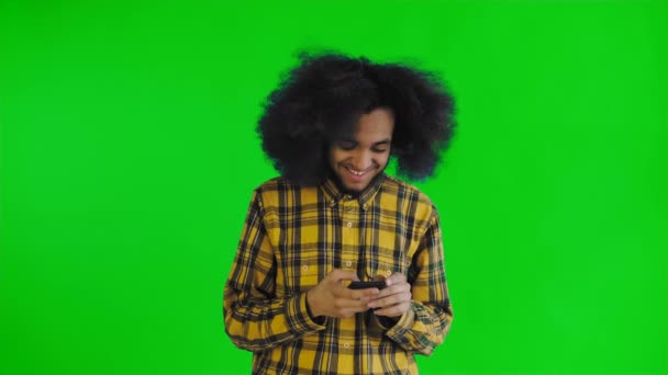 Ritratto di uomo afroamericano con capelli ricci che chatta su smartphone su schermo verde o sfondo cromatico. Concetto di emozioni — Video Stock