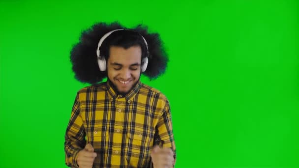 肯定的なアフリカ系アメリカ人の男性は、緑色の画面やクロマキーの背景に彼のヘッドフォンで音楽を聴いています。感情の概念 — ストック動画