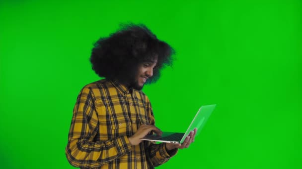 Hombre afroamericano feliz usando el ordenador portátil, sonriendo y desaparece en la pantalla verde o croma clave de fondo. Concepto de emociones — Vídeos de Stock