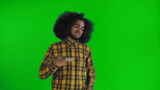 Hombre afroamericano satisfecho sosteniendo ventilador de billetes de dinero en sus manos y mirando a la cámara mientras está de pie aislado en la pantalla verde o croma clave de fondo — Vídeo de stock