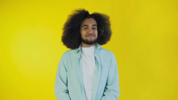 Fiatal afro-amerikai férfi mosolyog, néz és beszél a kamerába sárga háttérrel. Az érzelmek fogalma — Stock videók
