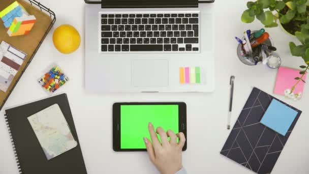 Ofis masasının üst görüntüsü ve üzerinde yeşil ekran ve kadın eli olan beyaz tablet bilgisayar.. — Stok video