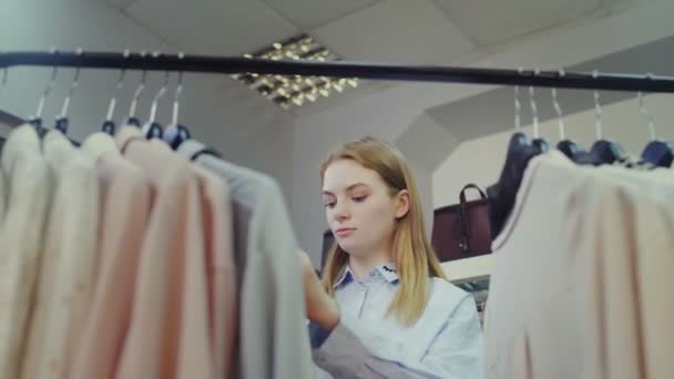 Junge Frau schaut auf Kleidung, hängt an Kleiderbügeln. — Stockvideo