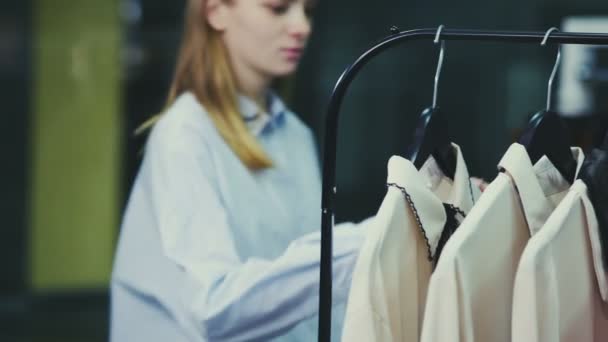 Dolly shot van Woman bladeren blouses op hangers. — Stockvideo