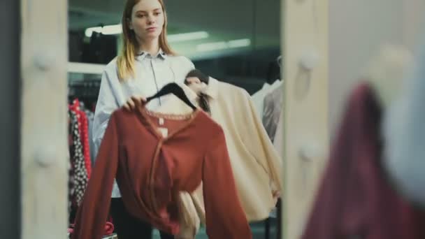 Cliente feminino atraente está escolhendo blusa no quarto de montagem — Vídeo de Stock