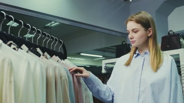 Mladá hezká dívka v butiku výběru oblečení na nákup. — Stock video