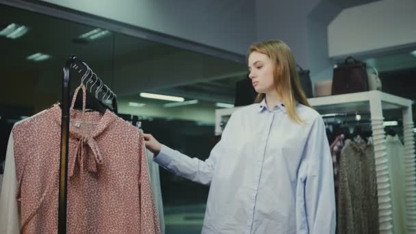 Woman shopping look over dresses on hangers in fashionable clothes boutique shop — Stock Video