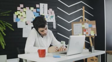 Bilgisayarlı genç işadamı cep telefonuyla konuşuyor ve notlar yazıyor.