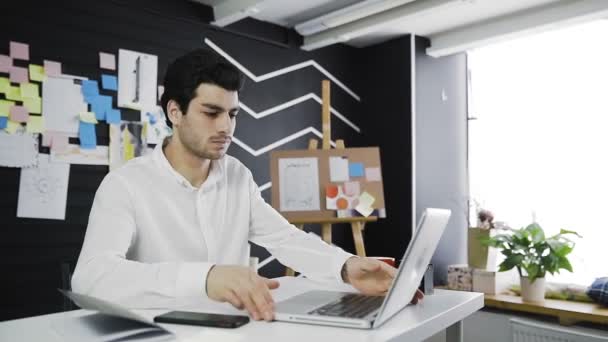 Dolly shot de jeune homme d'affaires tapant sur son clavier d'ordinateur portable dans un bureau loft — Video