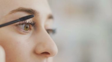 Güzel bir kadının siyah maskarayla göz makyajı yapıp aynaya baktığı yakın plan.