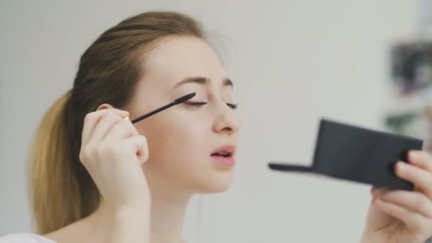Mulher fazendo maquiagem de olhos por rímel preto, olhando para o espelho — Vídeo de Stock