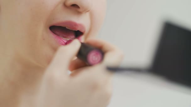 Close-up vrouwelijke lippen met lippenstift. Ze houdt een tube lippenstift in haar handen en kijkt naar de spiegel. — Stockvideo