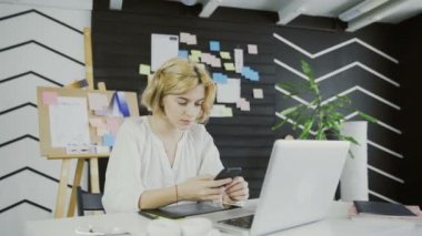 Ofiste akıllı telefon kullanarak Çekici kadın tasarımcı.