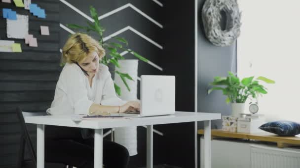 Meşgul iş kadını cep telefonu konuşuyor ve ofiste bilgisayar üzerinde çalışıyor — Stok video