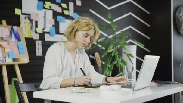 Γυναίκα σχεδιαστής που εργάζεται σε ένα φορητό υπολογιστή με ένα tablet γραφικών. — Αρχείο Βίντεο