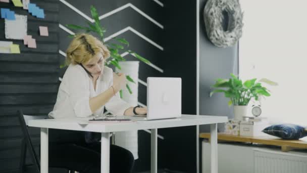 Young businesswoman is talking on her smartphone while working on notebook — Stock Video